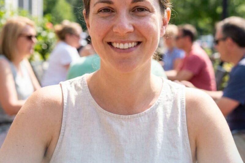 Smiling woman outdoors at a social event on a sunny day.