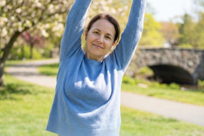 Woman stretching in a sunny park setting.