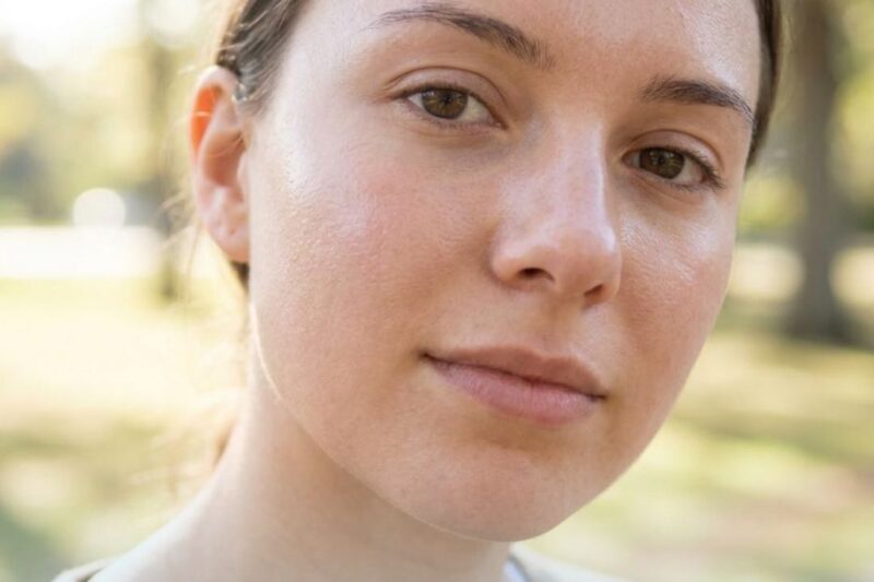 Close-up of a woman with smooth, clear skin in natural light outdoors.